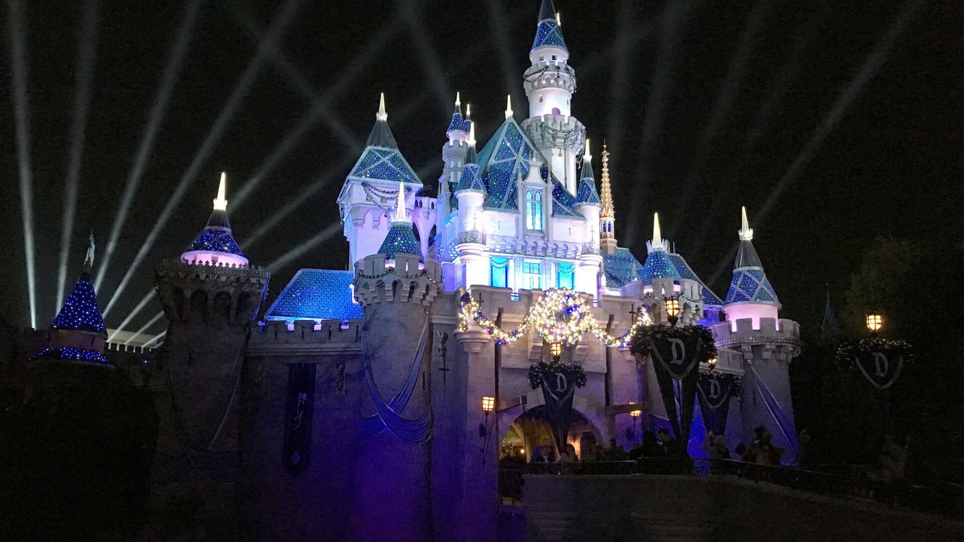Castillo de Disneyland iluminado de noche con focos cruzando el cielo